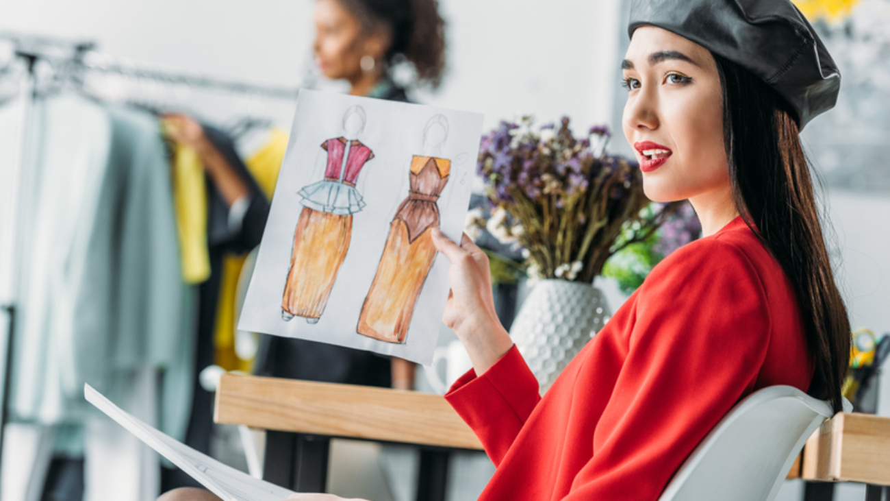 attractive young asian fashion designer holding sketches and looking away