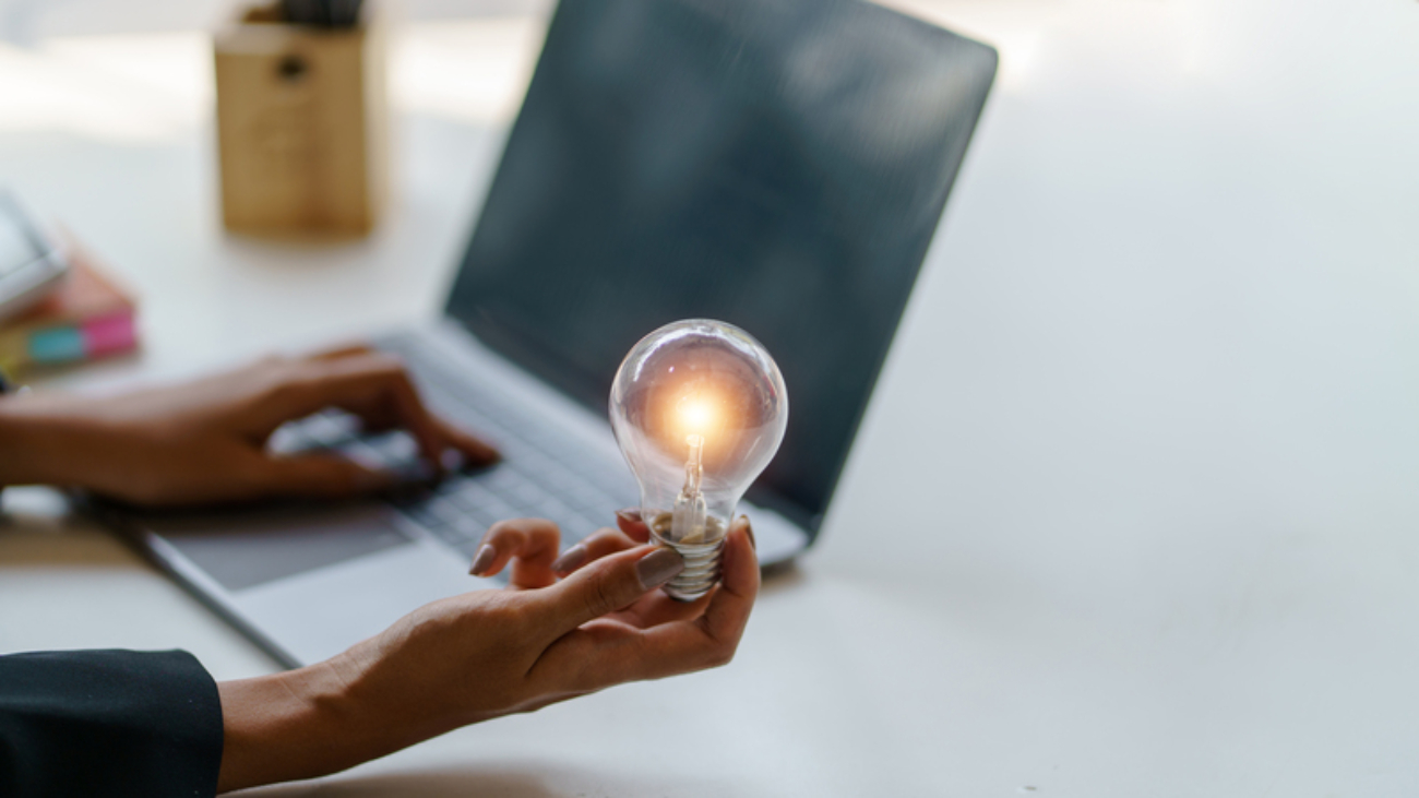Businesswoman typing on laptop keyboard and holding illuminated light bulb in her hand, symbolizing new ideas, innovation and creativity in business