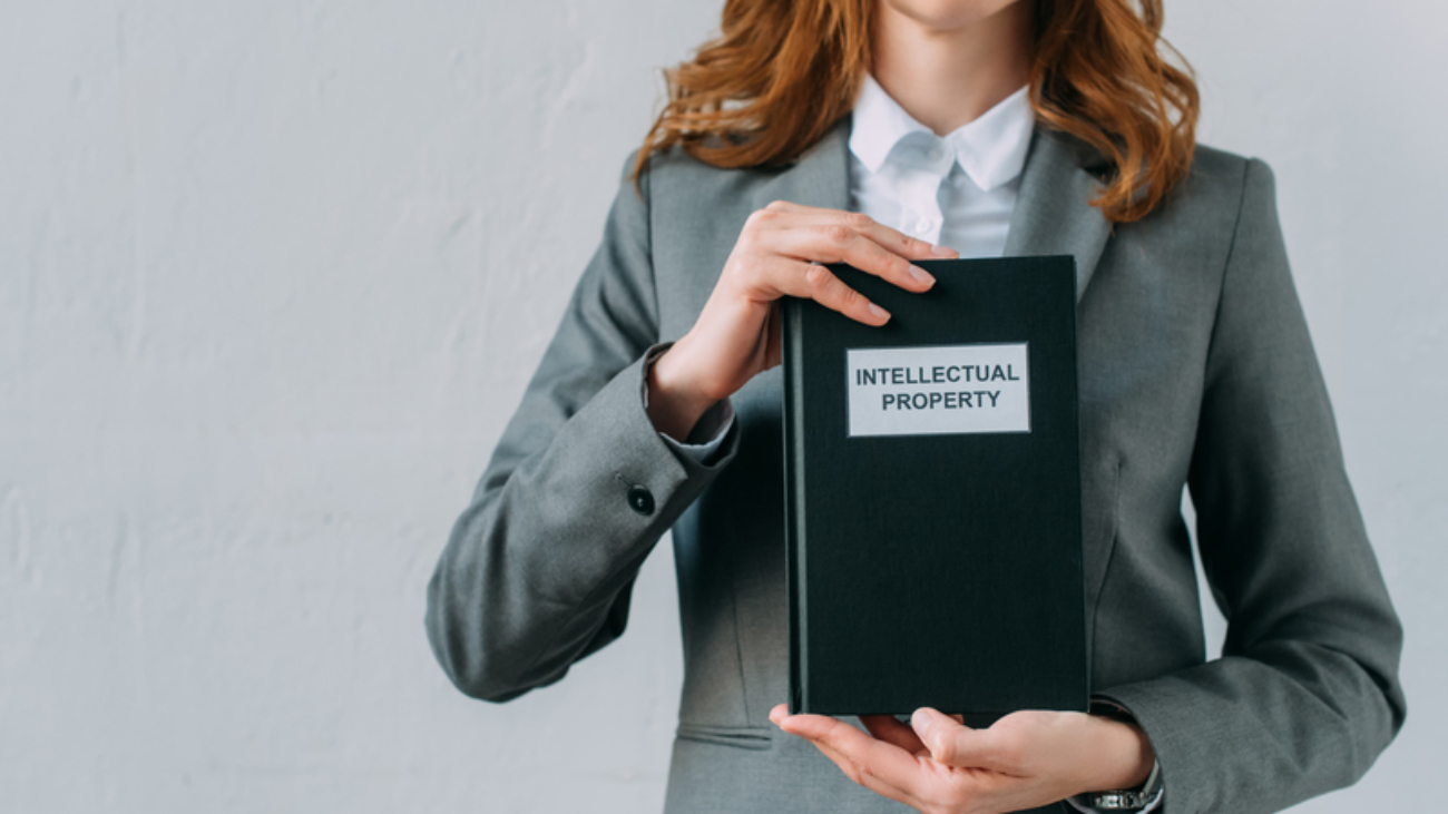 Cropped view of female lawyer holding book with intellectual property lettering on grey