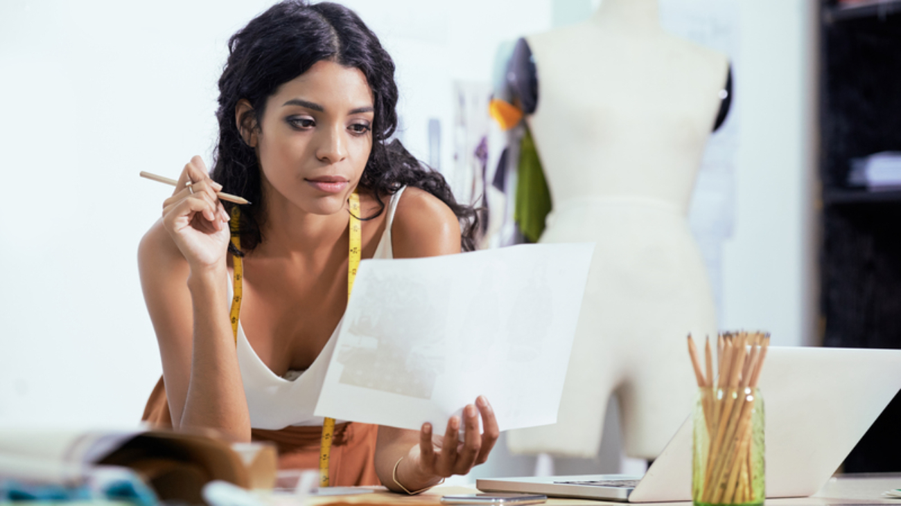 Beautiful young woman drawing sketch while working on a new collection of clothes in studio