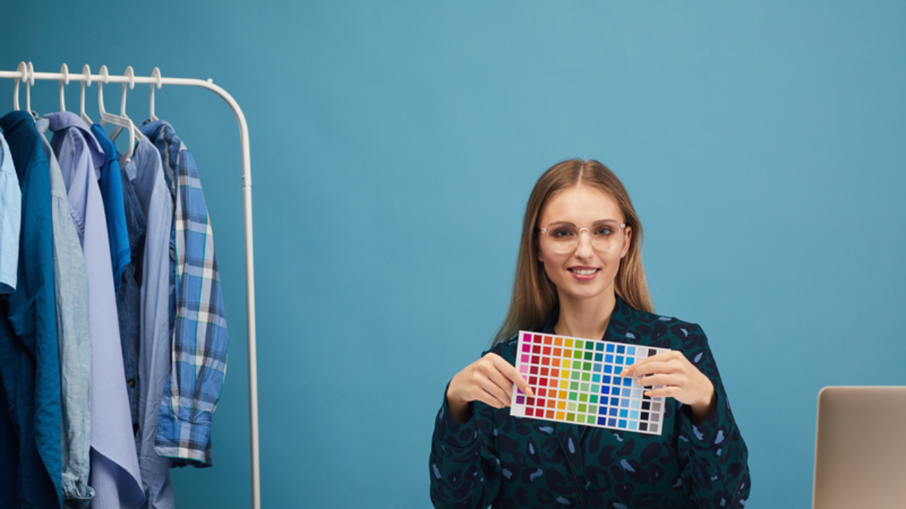Portrait of young woman sitting at the table showing colored pattern and smiling at camera while working at studio