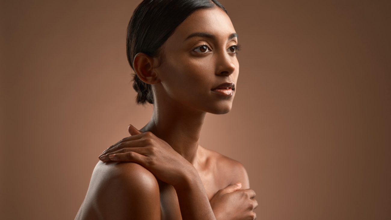 Side shot of a beautiful young woman posing against a brown background.